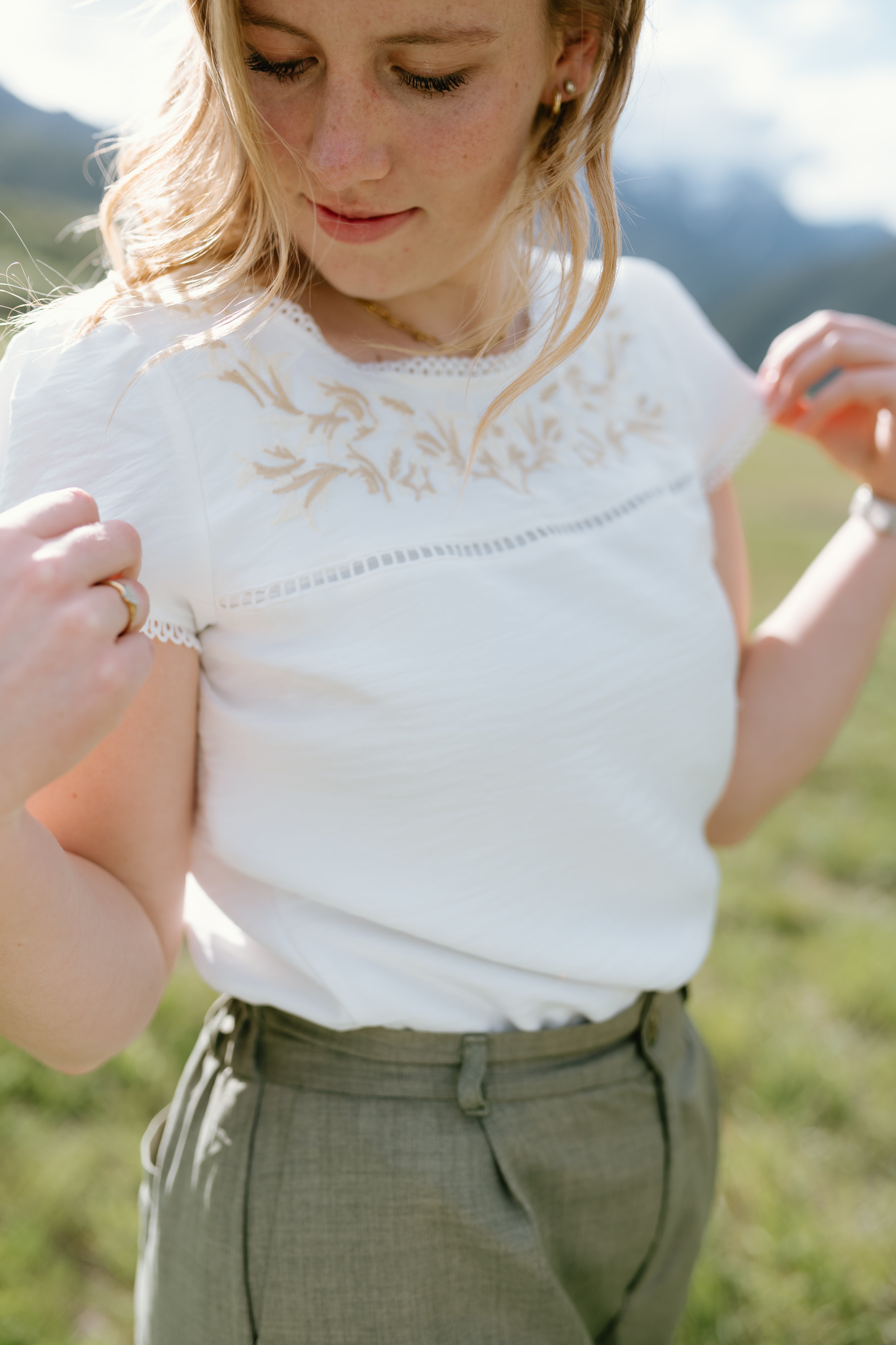 Light-colored Hampton Top with embroidered details and lace trim, worn casually outdoors.