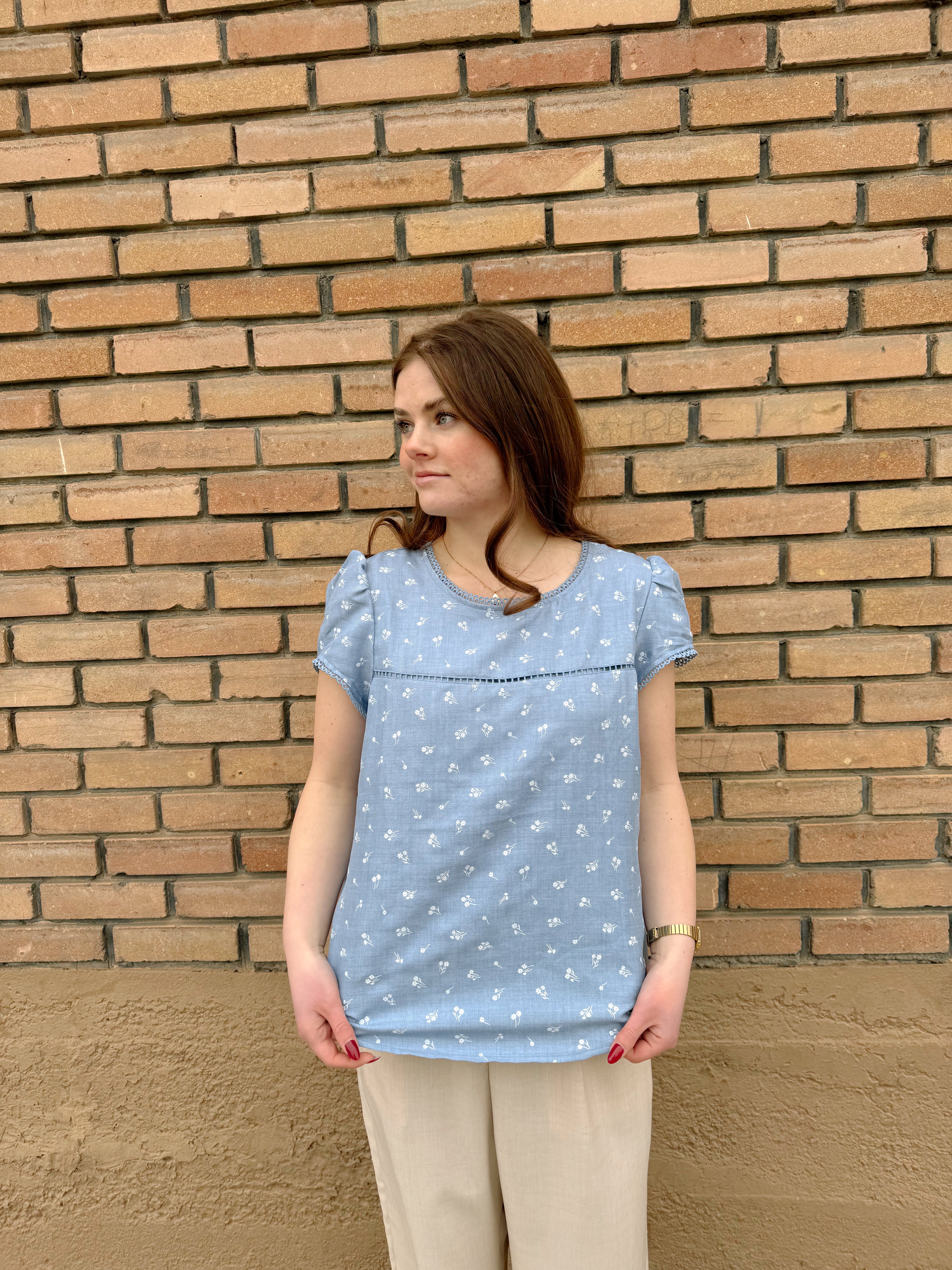 Light blue Hampton Top with white floral pattern, puff sleeves, and delicate trim, styled with beige pants.