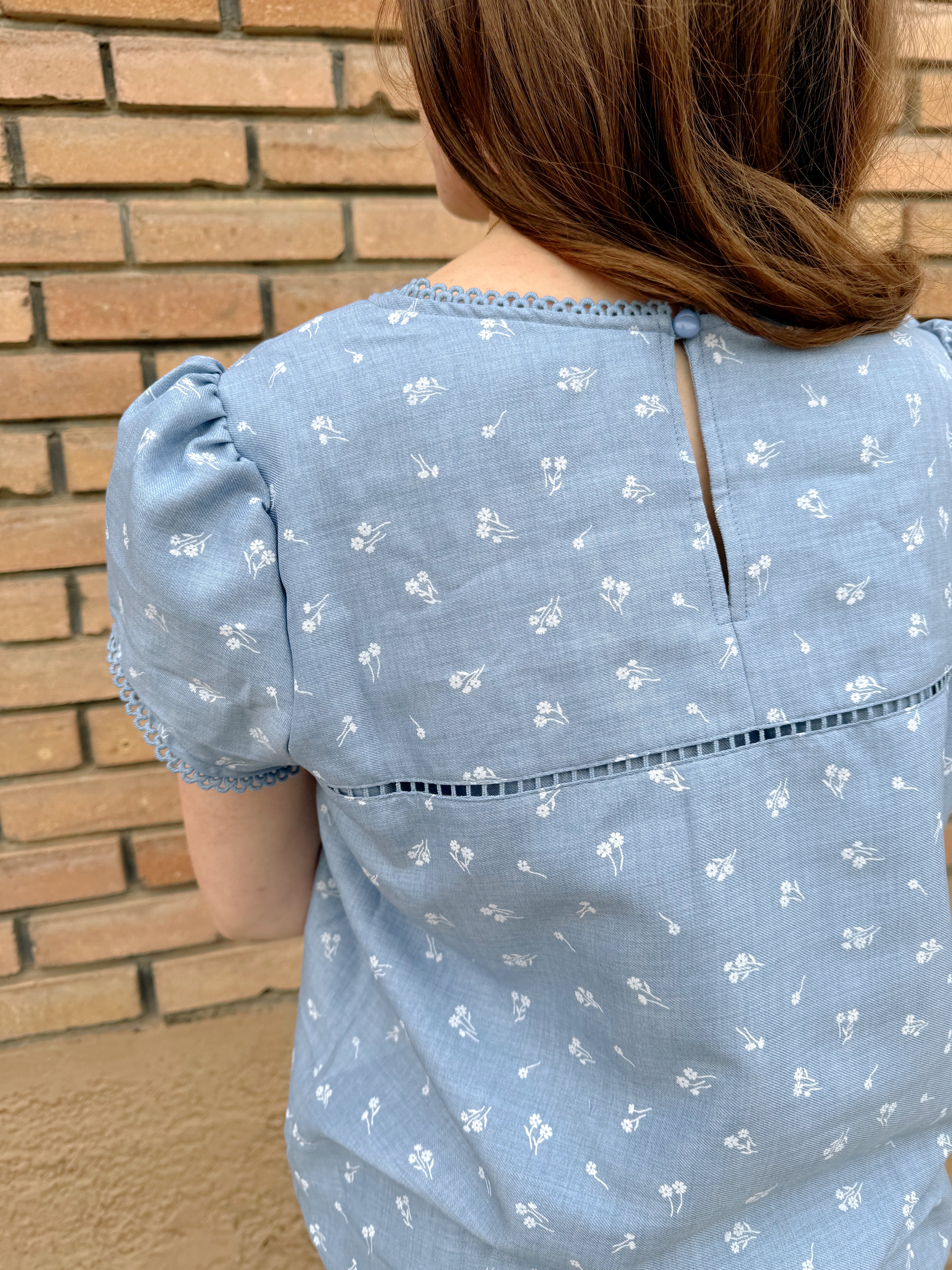 Soft blue Hampton Top with white floral print and delicate lace trim, perfect for casual or dressy occasions.